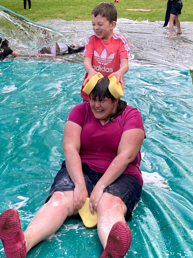 Image of a female adult volunteer being soaked by water and wet sponges by a smiling child